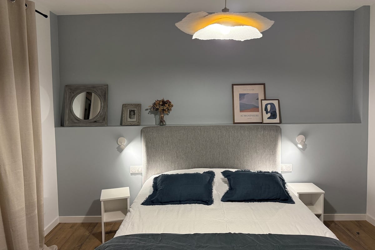 A bedroom with a bed, bedside tables, a hanging light fixture, and wall-mounted artwork.