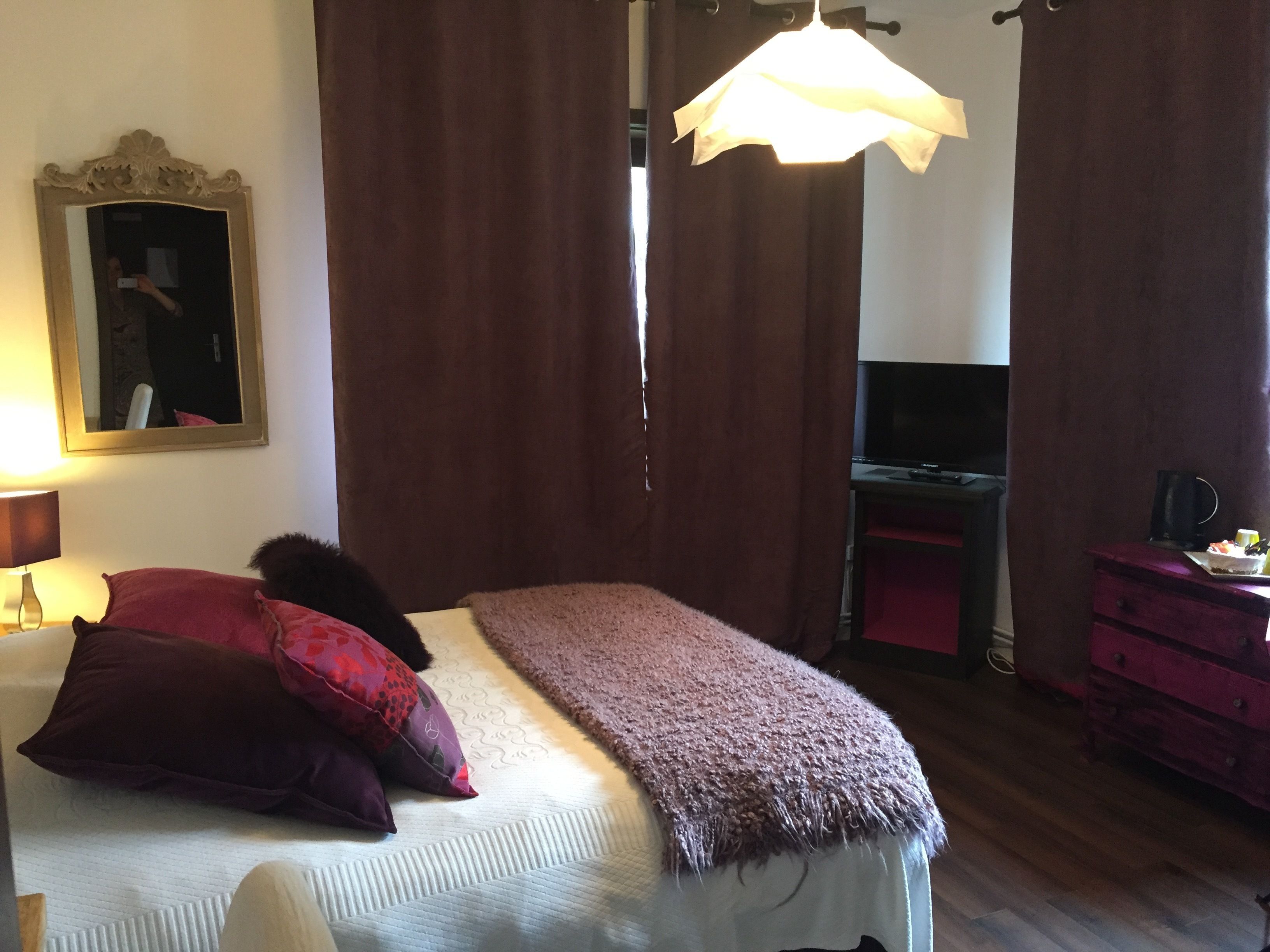 A bedroom with a bed, a mirror, a TV, and a dresser.