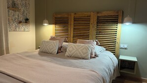 Un dormitorio con una cama grande, cabecera de madera, dos mesitas de noche y una estantería en la pared.