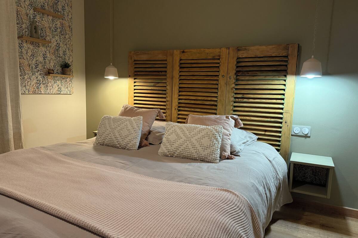 A bedroom with a large bed, wooden headboard, two bedside tables, and a wall-mounted shelf.