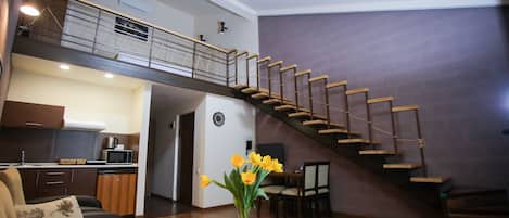 A spacious living area with a wooden staircase, a dining table, and a kitchen in the background.