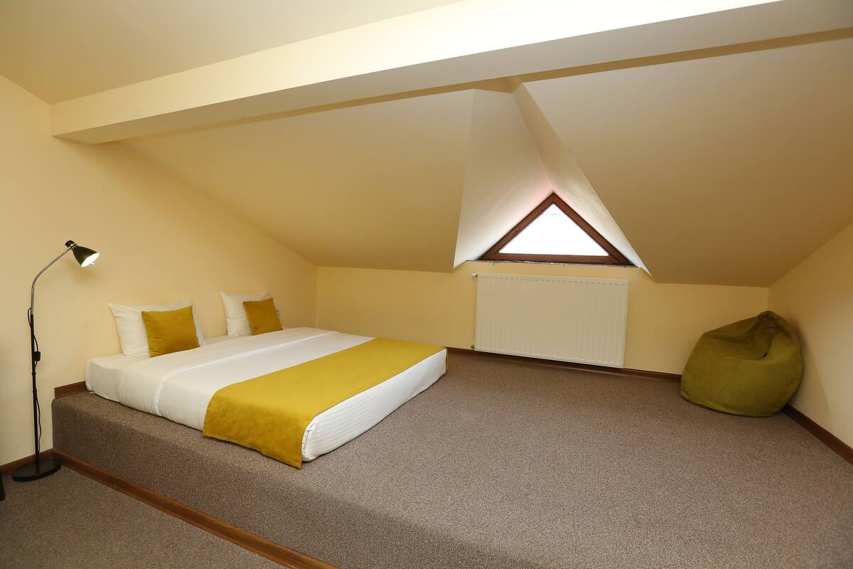 A bedroom with a bed, a green bean bag, a lamp, and a skylight.