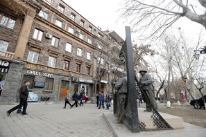 A public square with a statue, a building with a sign, and people walking. - My Apartments Yerevan (Yerevan)