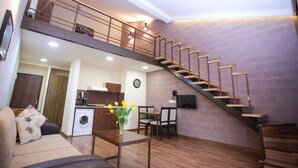 A spacious living area with a wooden staircase, a sofa, a coffee table with flowers, a washing machine, and a dining area. - My Apartments Yerevan (Yerevan)