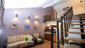 A modern living room with a sofa, coffee table, and a vase of flowers. There is a staircase with a wooden railing leading to an upper level. - My Apartments Yerevan (Yerevan)