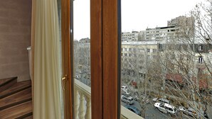 A view from a window with a wooden frame and a curtain, overlooking a cityscape with buildings and parked cars. - My Apartments Yerevan (Yerevan)