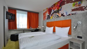 A hotel room with a bed, a desk, a chair, a TV, and a window with curtains.