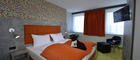 Habitación de hotel moderna con una cama grande, un escritorio, una silla, un televisor y un papel tapiz estampado.