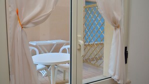 A sliding glass door with white curtains, leading to an outdoor balcony with a white table and chairs. - Residence Verbena (Rimini)