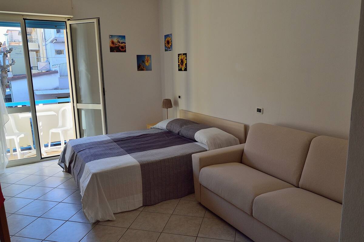 Quarto com cama, sofá e vista para a varanda.