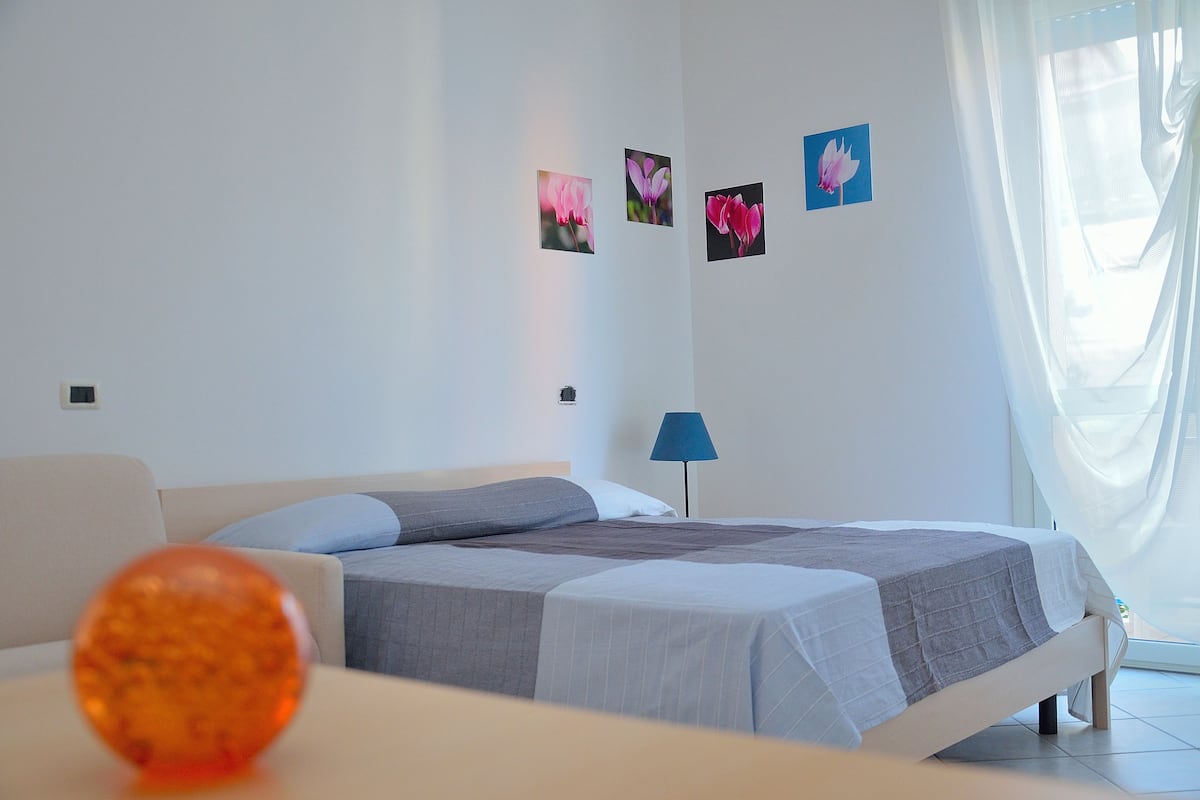 Quarto de hotel moderno com cama, mesa de cabeceira, abajur e obras de arte nas paredes.