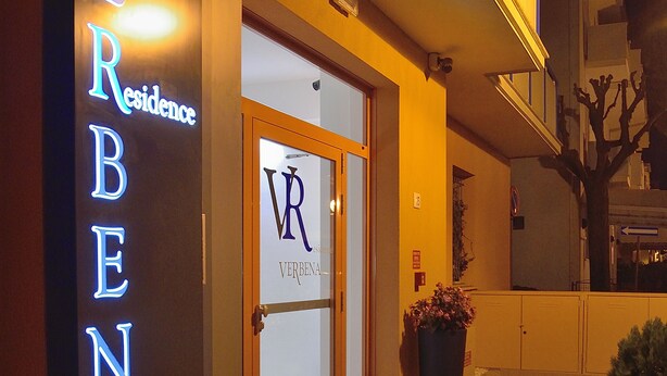 A hotel entrance with illuminated signage reading "VERBENA Residence" and a glass door with a logo. - Residence Verbena (Rimini)