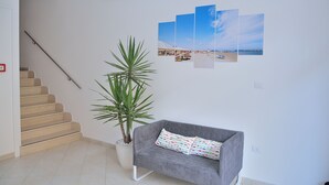 A staircase, a gray sofa with patterned cushions, a potted plant, and a wall with a beach scene artwork. - Residence Verbena (Rimini)