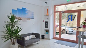 A reception area with a grey sofa, a large potted plant, and a framed artwork on the wall. - Residence Verbena (Rimini)