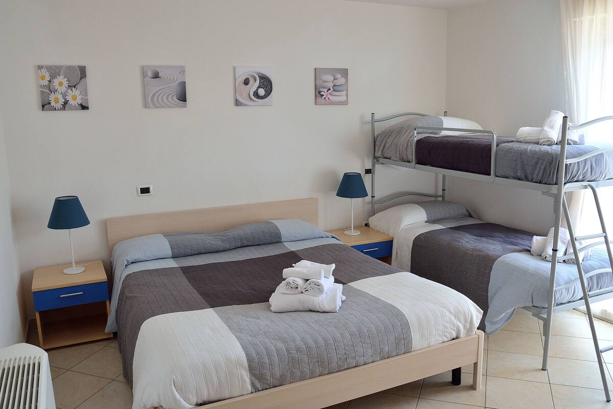 Quarto de hotel com duas camas, incluindo uma beliche, uma mesa de cabeceira com abajur e obras de arte na parede.