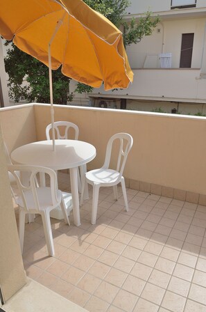 A balcony with a white table and chairs, an orange umbrella, and a tiled floor. - Residence Verbena (Rimini)