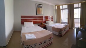 Quarto de hotel com duas camas, uma mesa de cabeceira e uma janela com cortinas.
