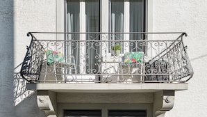Un edificio de dos pisos con balcones, cada uno con barandilla de metal y plantas en macetas.