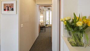 Un pasillo con un retrato enmarcado en la pared, una planta en maceta y un jarrón con flores amarillas.
