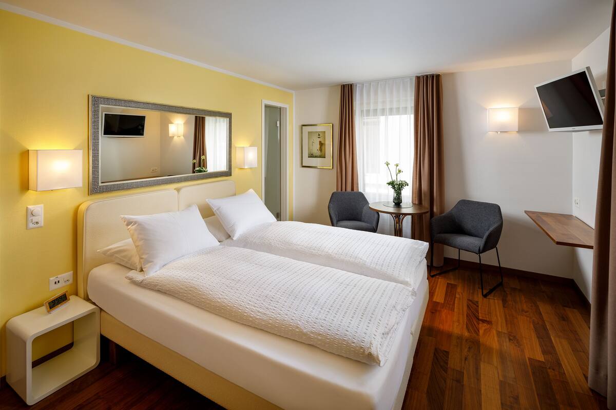 A hotel room with two beds, a desk, a chair, a TV, and a window with curtains.