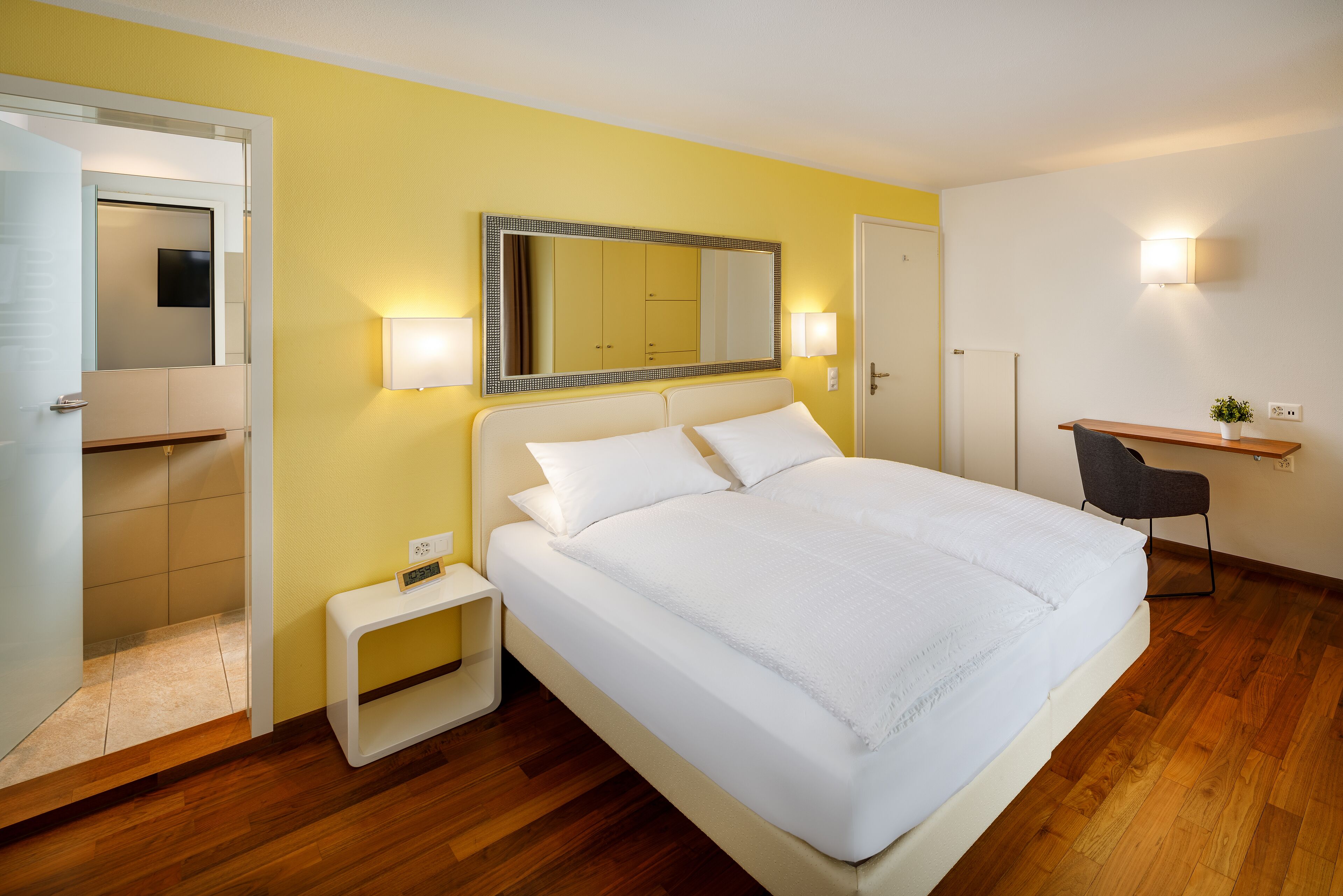 Ein Hotelzimmer mit einem großen Bett, einem Nachttisch und einem Schreibtisch mit Stuhl.