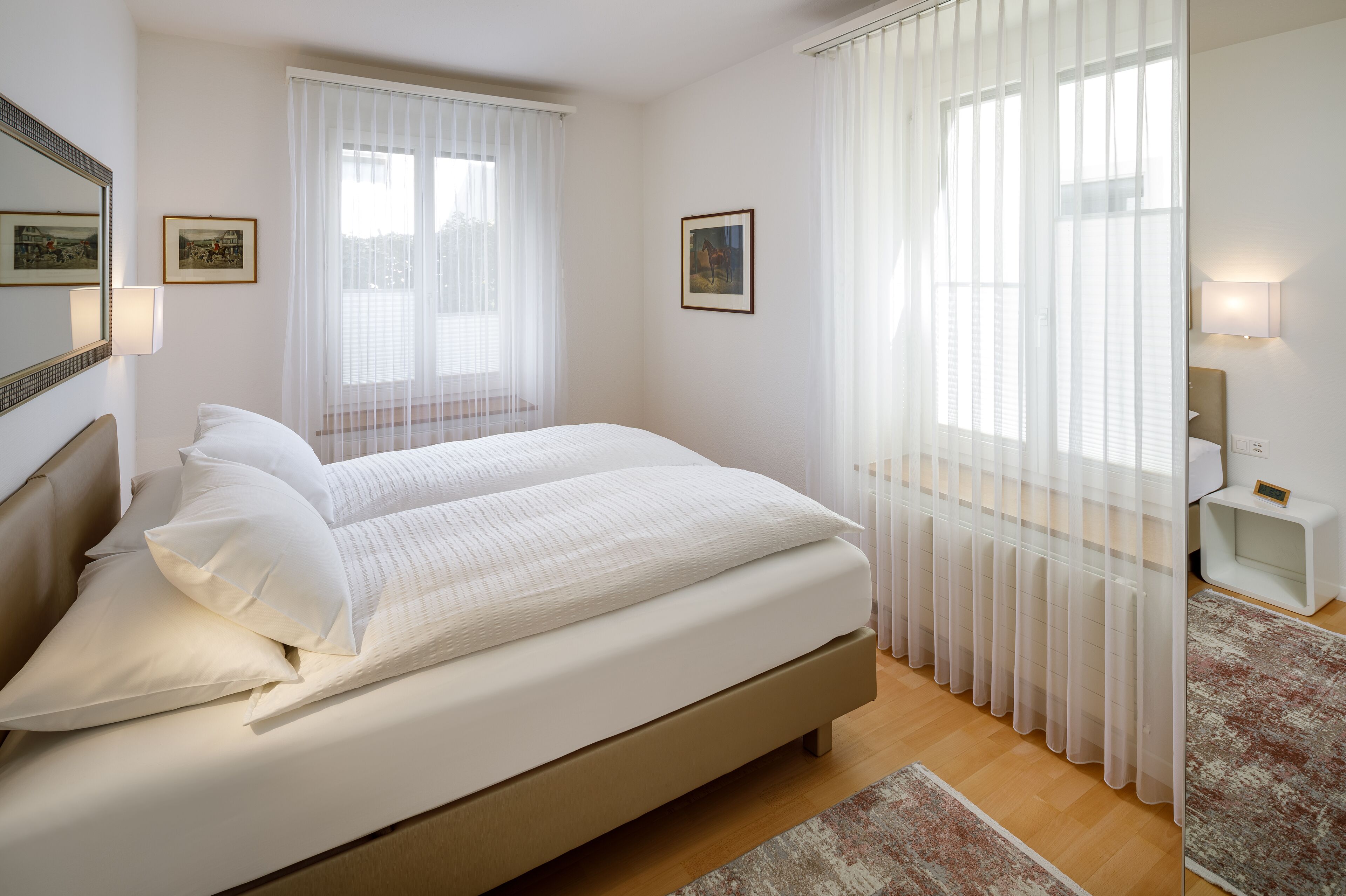 Ein Schlafzimmer mit einem großen Bett, zwei Nachttischen, einem Beistelltisch und einem Fenster mit durchsichtigen Vorhängen.