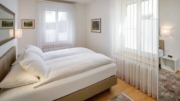 Ein Schlafzimmer mit einem großen Bett, zwei Nachttischen, einem Beistelltisch und einem Fenster mit durchsichtigen Vorhängen.