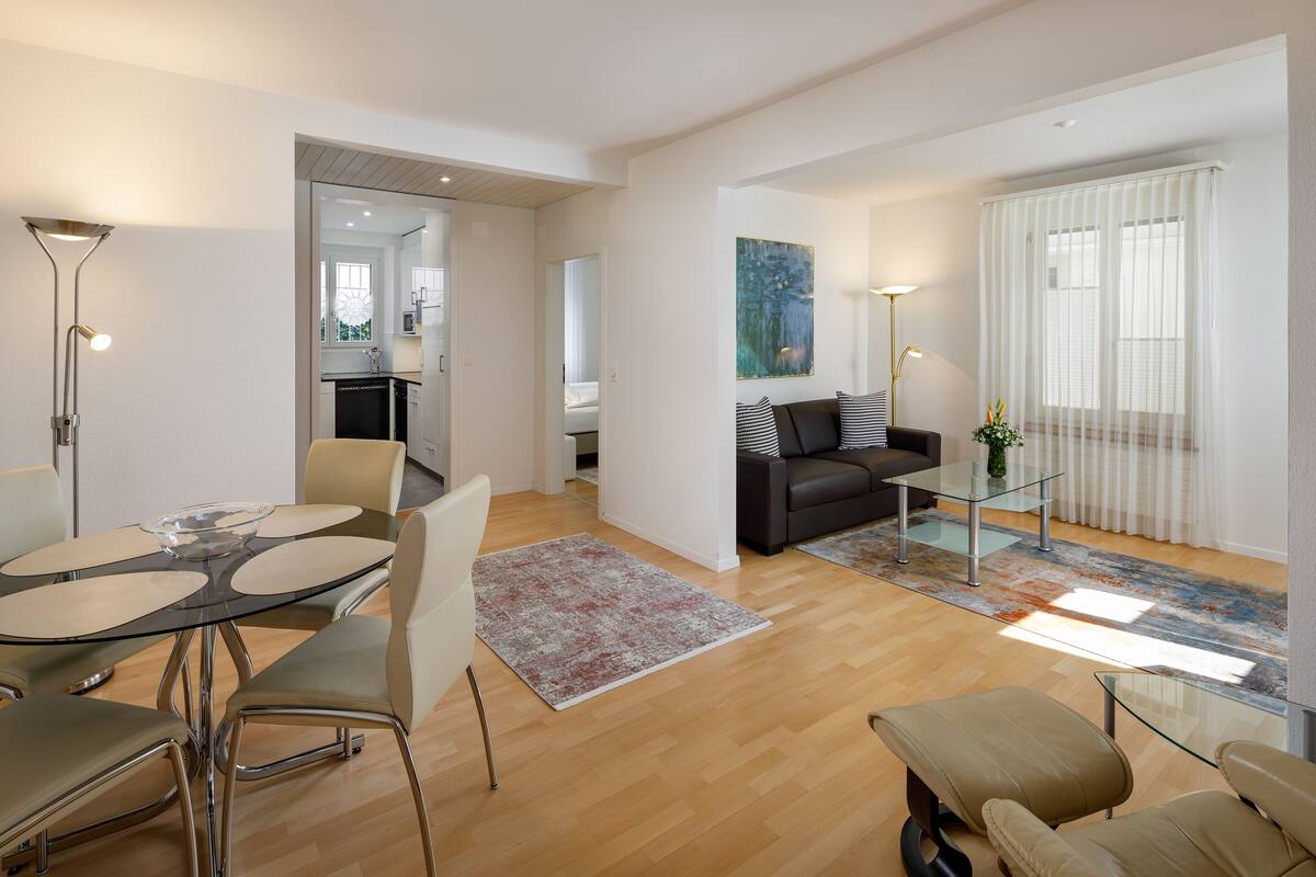 A modern living room with a glass coffee table, a sofa, and a dining area with a glass table and chairs.