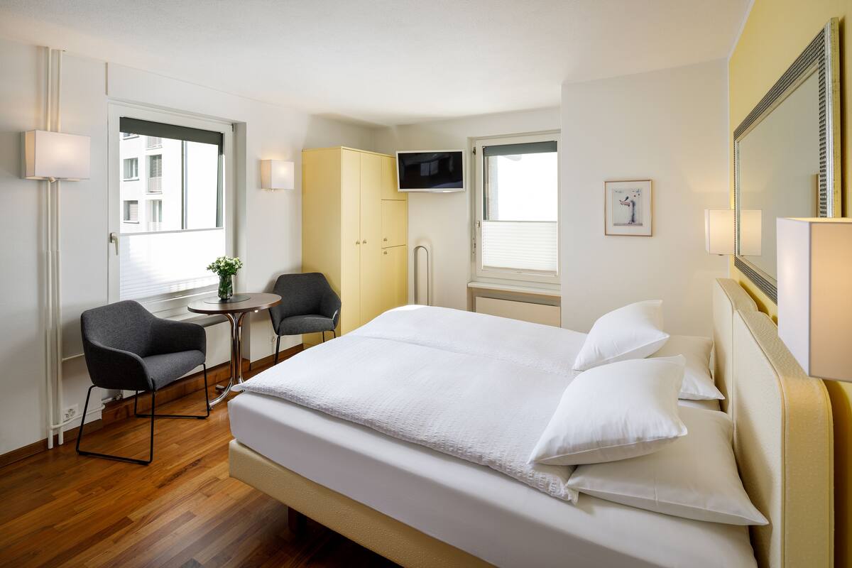 A hotel room with a bed, a desk, a chair, a TV, and a window.