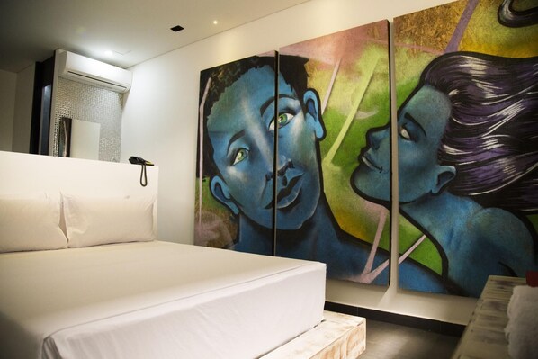 Un dormitorio con cama, aire acondicionado de pared y un cuadro abstracto grande.