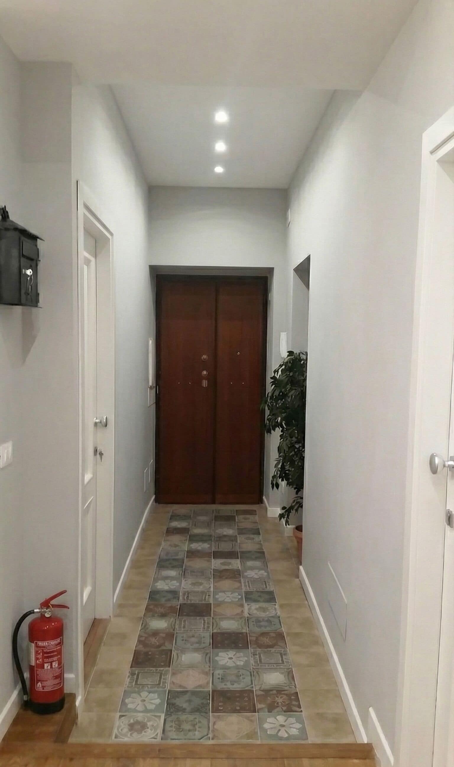 A hallway with a tiled floor, a wooden door at the end, and a fire extinguisher on the left.