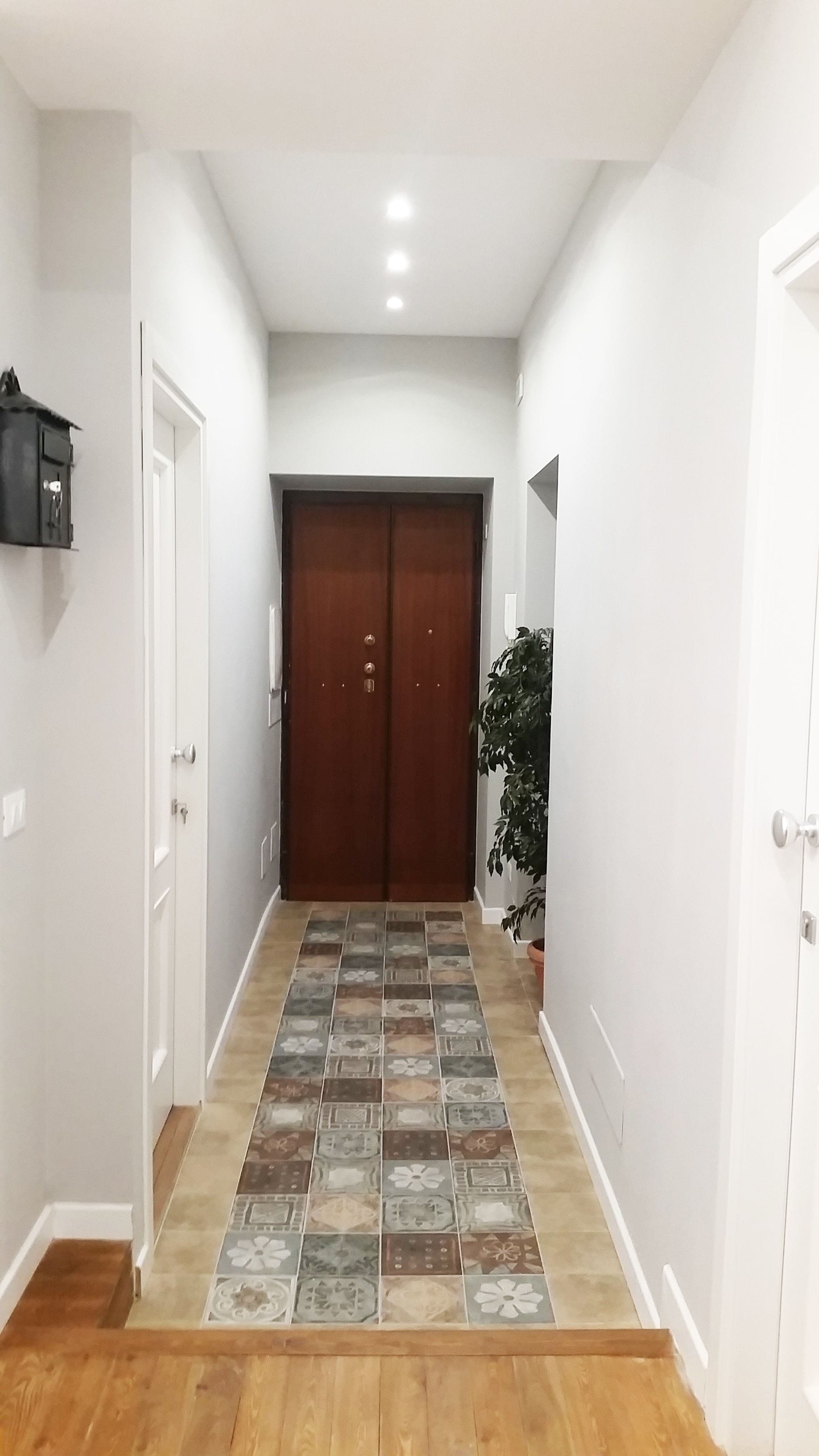 A hallway with a tiled floor, a wooden door at the end, and a potted plant on the right.