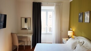 A hotel room with a bed, a desk, a chair, a TV, a window with curtains, and a nightstand with a lamp. - MORE Cola di Rienzo B&B (Rome)