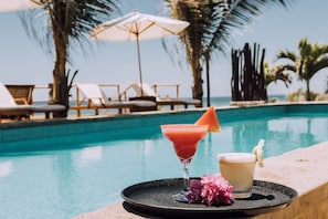 A poolside setting with lounge chairs, a drink tray with two cocktails, and a view of the ocean.