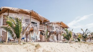 Una propietat a peu de platja amb edificis de teulada de palla, palmeres i gandules.