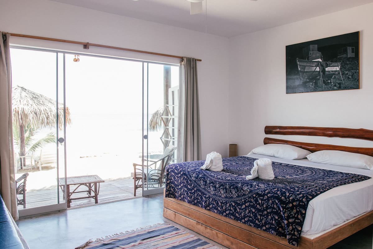 A bedroom with a large bed, a view of the beach through a sliding glass door, and a painting on the wall.