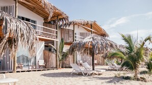 Un hotel a la vora de la platja amb construccions de teules de palla, gandules blanques i palmeres.