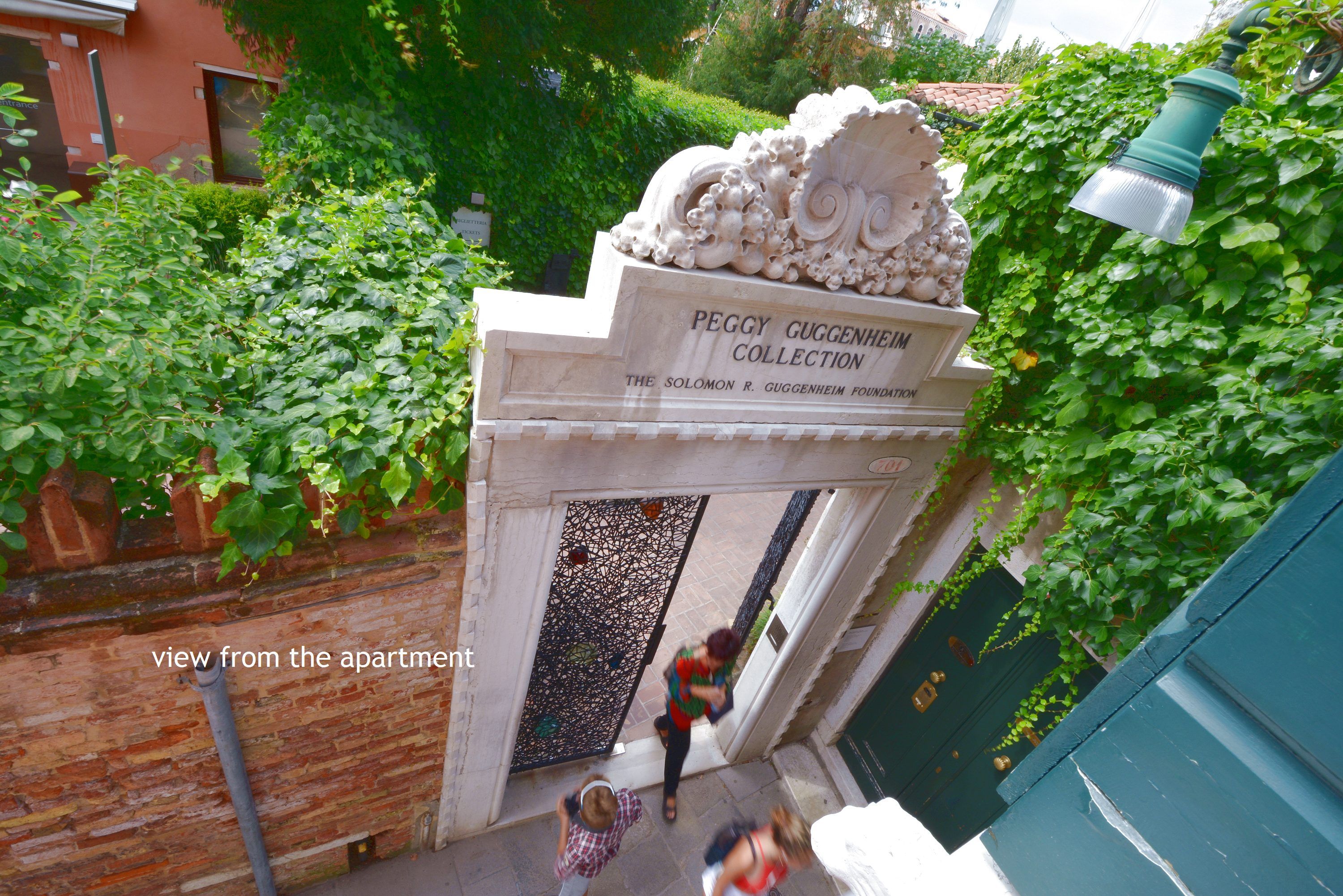 An entrance to the Peggy Guggenheim Collection with a stone archway and a decorative sculpture.