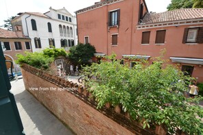 A view from an apartment overlooking a narrow street with a brick wall and a row of potted plants. - PEGGY-Guggenheim (Venice)