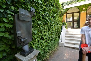 En skulptur som föreställer ett ansikte med abstrakta drag, en grön vägg täckt av murgröna och en byggnadsentré med trappsteg.
