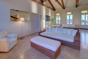 Un salón amplio con un sofá grande de mimbre, un sillón blanco y una lámpara de pie.
