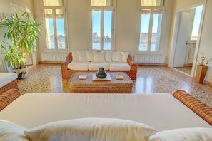 Una habitación amplia con una cama grande, un sofá de mimbre y vistas de la ciudad a través de amplias ventanas.