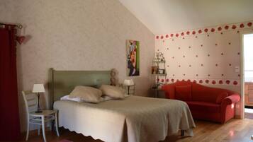 Un dormitorio con cama, sofá rojo, silla, mesita de noche, lámpara y un papel tapiz floral en la pared.