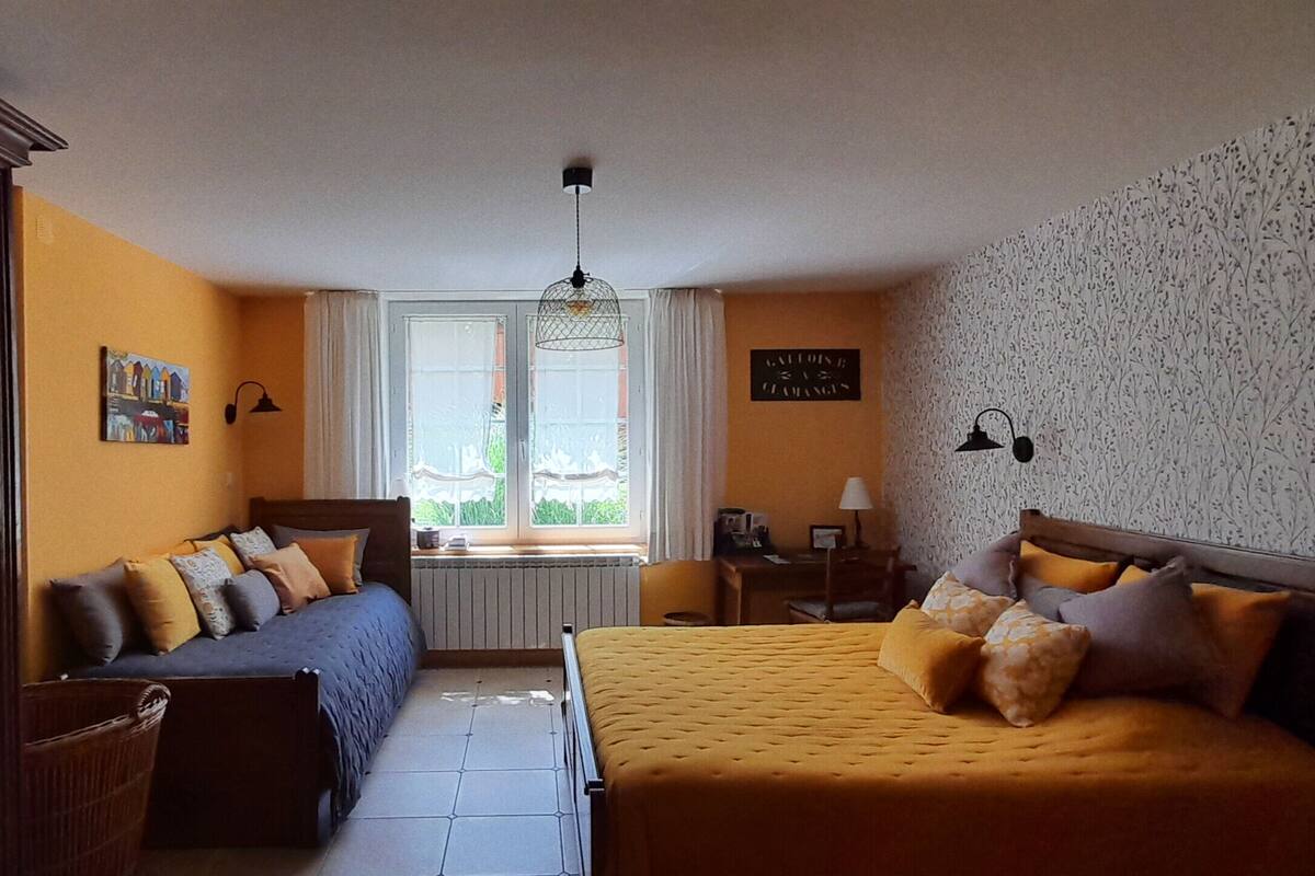 Un dormitorio con dos camas, una ventana con cortinas, un radiador, un escritorio con lámpara y una pared con estampado floral.