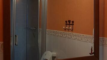 A bathroom with a large mirror, a sink with a soap dispenser, and a shower visible in the background.