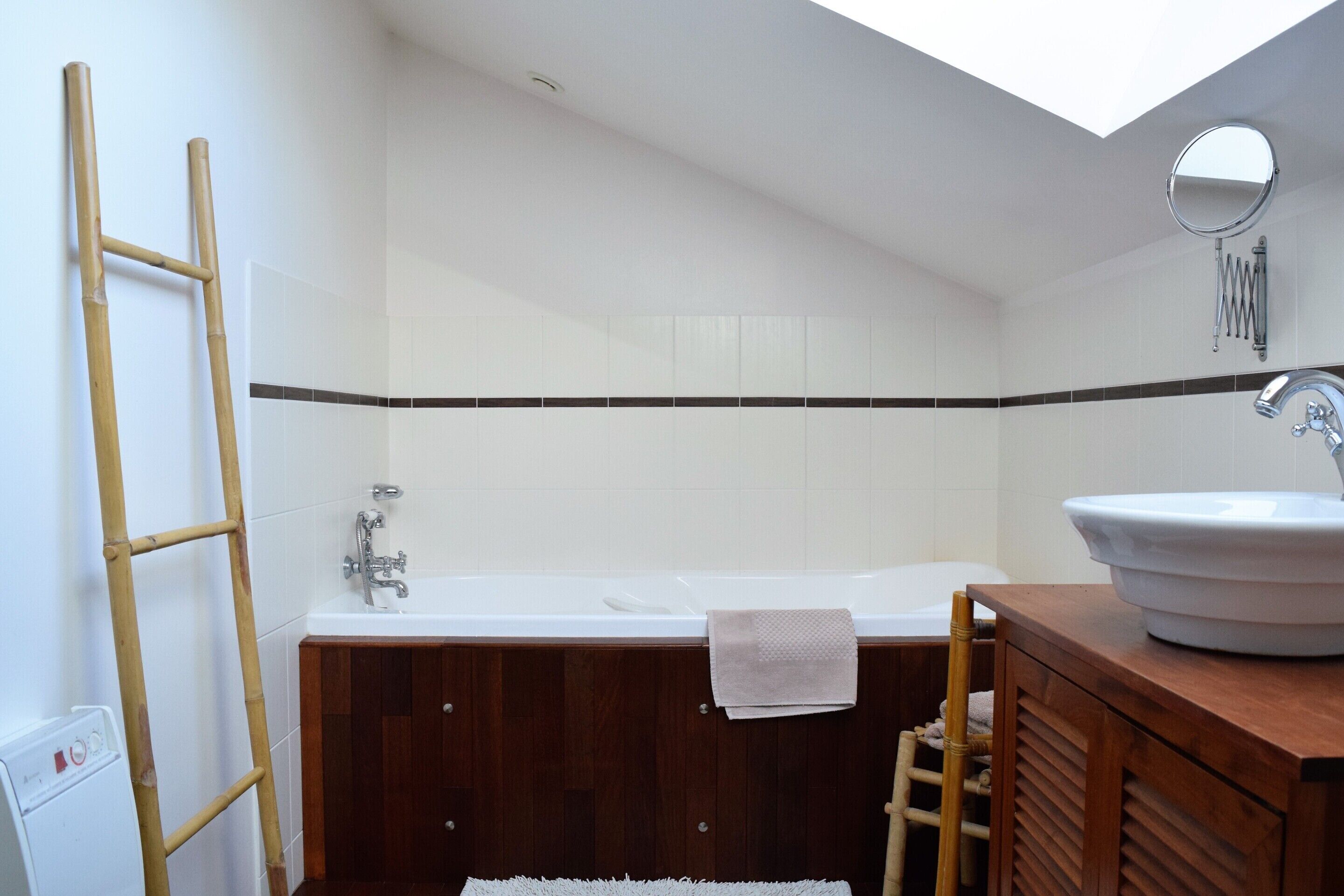 A modern bathroom with a wooden vanity, a white bathtub, and a skylight.