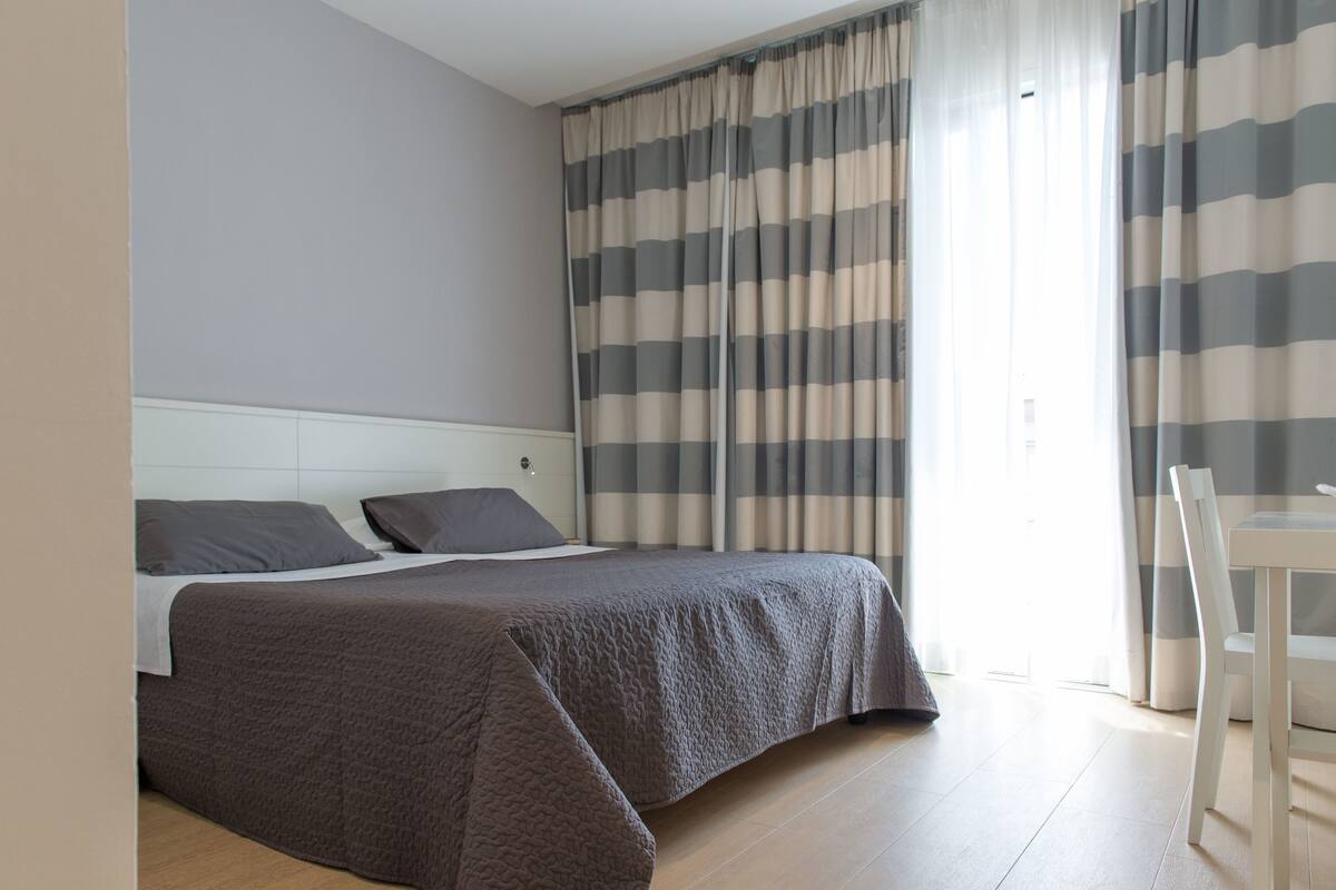 A modern hotel room with a large bed, a bedside table, and a chair.