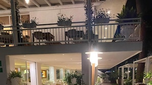 Une terrasse en bois agrémentée de plantes en pot et d’un banc, qui mène à un espace restaurant doté de tables en plein air.