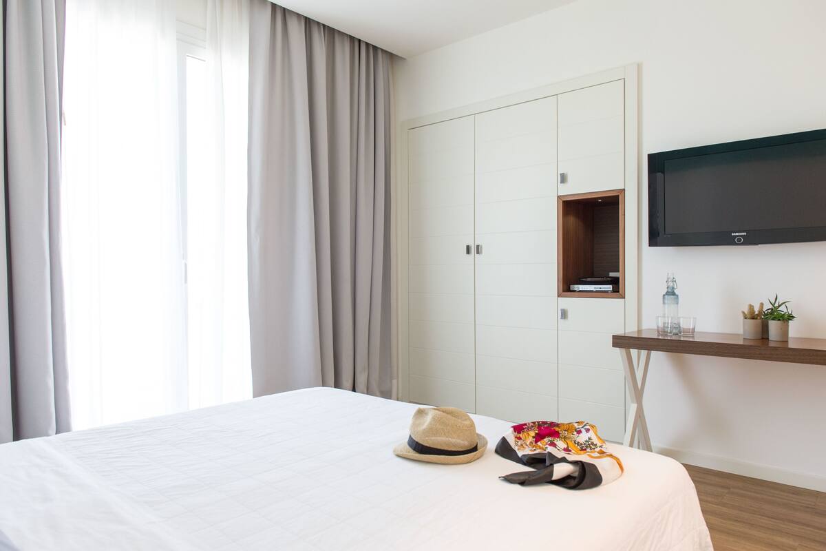 A hotel room with a bed, a wardrobe, a TV mounted on the wall, and a small shelf with decorative items.