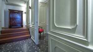 A hallway with a wooden staircase, a red chair, and a door with decorative molding. - GRITTI Grand Canal (Venice)